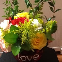 Bouquet of red, yellow, and white roses with greenery in a gift bag