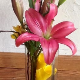 Pink lilies in a clear rectangular vase with yellow petals inside