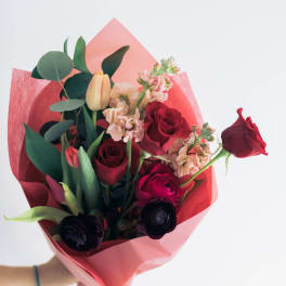 Bouquet of red roses, tulips, and pale pink flowers wrapped in pink paper