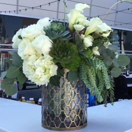 White roses and calla lilies arranged with succulents in a patterned metal vase
