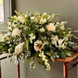 Low centerpiece of cream roses and white flowers with abundant greenery on a wooden table