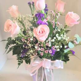 Pink roses and purple filler flowers in a clear vase with a pink ribbon