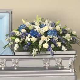 Large white and blue casket spray with roses, lilies, and hydrangeas on a silver casket.