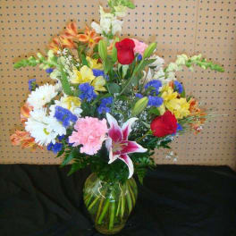 Mixed bouquet of lilies, roses, daisies, and carnations in a glass vase