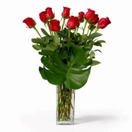 Red roses in a clear glass vase with large green leaves