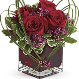 Red roses and purple filler in a square glass vase