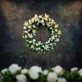 White floral wreath on a stand with lilies and small daisies