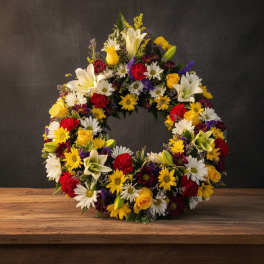 Circular floral wreath with mixed daisies, roses, lilies, and carnations