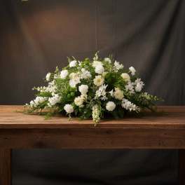 Low white floral arrangement with mixed blooms on a wooden table