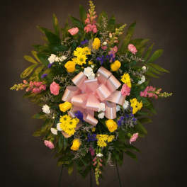 Standing floral spray with yellow, pink, white, and purple flowers and a pink bow