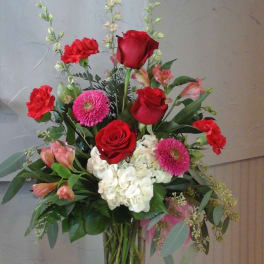 Mixed bouquet of red roses, pink blooms, and white hydrangea in a glass vase