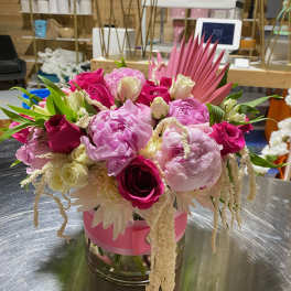Low pink and white arrangement with peonies and roses in a glass vase wrapped with pink ribbon