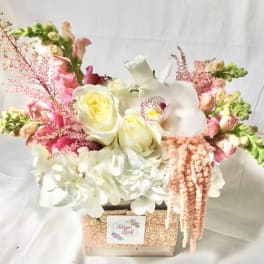 Pink and white floral arrangement in a glittery box with cascading blooms