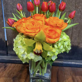 Orange roses and red tulips arranged in a clear glass vase