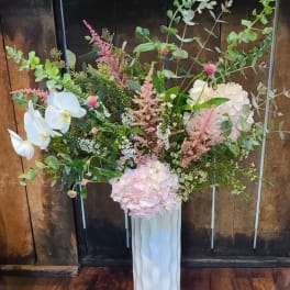 Tall floral arrangement with pale pink hydrangeas and white orchids in a white vase