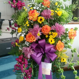 Tall floral standing spray with orange roses, purple mums, and yellow daisies