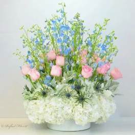 Pink roses and blue delphinium in a white vase with white hydrangeas