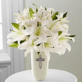 White lilies arranged in a tall cream vase with a cross emblem