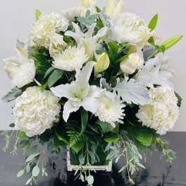 White floral arrangement in a square container with trailing greenery