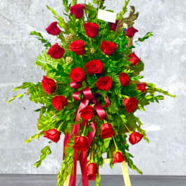 Standing spray of red roses with a pink ribbon on a tripod easel