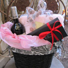 Gift basket with a wine bottle, wrapped box, and black gift box with red ribbon