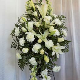 White floral standing spray with lilies and carnations on a black easel