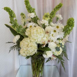 White floral arrangement in a clear glass vase with tall green spikes