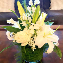 White lilies and roses in a glass vase with green foliage