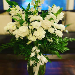 White flowers arranged in a tall glass vase with a ribbon bow