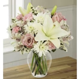 Bouquet of white lilies, pink roses, and white daisies in a clear glass vase