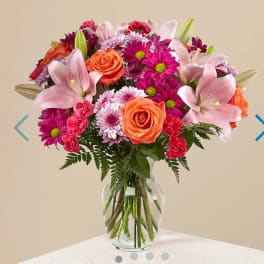 Mixed bouquet of pink lilies, orange roses, and magenta daisies in a glass vase