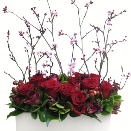 Red roses and pink blossoms arranged in a white rectangular container