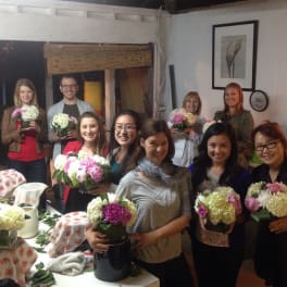 Group of people holding pink and white flower arrangements in a room