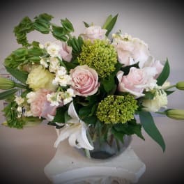 Pink and white roses arranged in a glass vase with green blooms