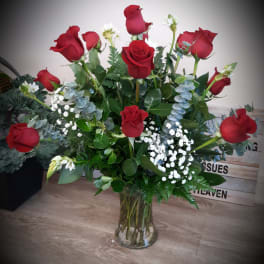 Tall arrangement of red roses with white filler flowers in a clear glass vase
