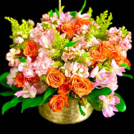 Orange roses and pink flowers arranged in a gold bowl