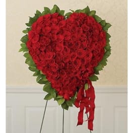 Heart-shaped arrangement of red roses with a green leaf border and red ribbon