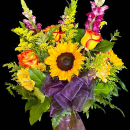 Bouquet of sunflowers, orange roses, and purple snapdragons in a glass vase