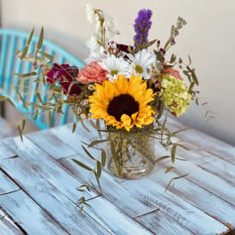 Mixed bouquet with a sunflower in a glass vase on a blue table