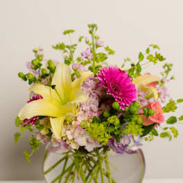 Mixed bouquet with yellow lilies, pink gerbera daisies, and roses in a glass vase