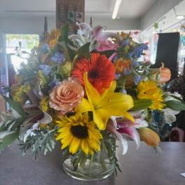 Mixed bouquet with lilies, roses, gerbera daisies, and sunflowers in a glass vase