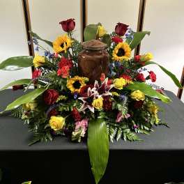 Large floral arrangement with roses, sunflowers, lilies, and a brown urn centerpiece