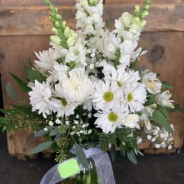 White daisies and snapdragons in a glass vase with greenery