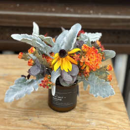 Small floral arrangement in a brown candle jar with yellow and orange blooms