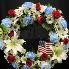 Circular wreath of red roses, white lilies, and blue carnations with a small American flag