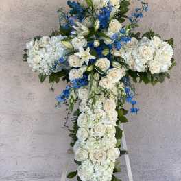 White floral cross arrangement with blue accents on an easel