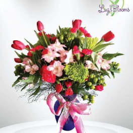 Bouquet of red tulips and pink lilies in a purple vase with a pink ribbon