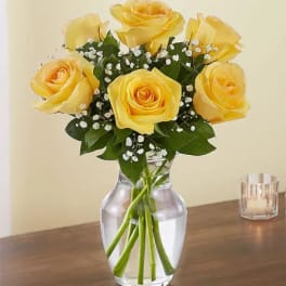 Yellow rose bouquet with baby's breath in a clear glass vase on a wooden table