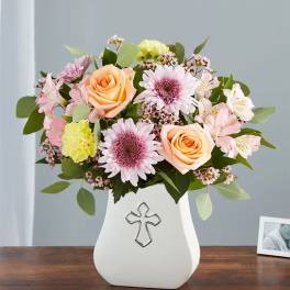Pastel flower arrangement in a white vase with a cross emblem