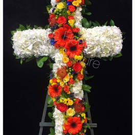 Floral cross arrangement with white blooms and bright mixed flowers on an easel